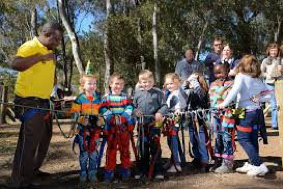A group of kids are getting all strapped up and ready to do some swinging through the trees at Acrobranch.  The kids are posing for a photo in their harnesses