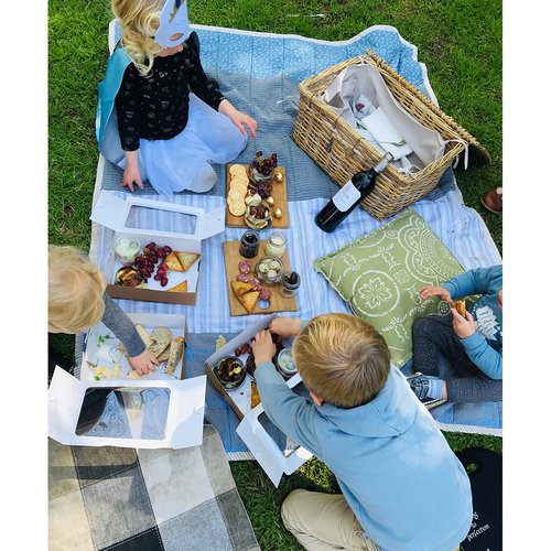 Children sitting on a blue blanket eating cheese and biscuits at Delheim Winery. Kids wearing maskd having fun at a picnic on the grass.