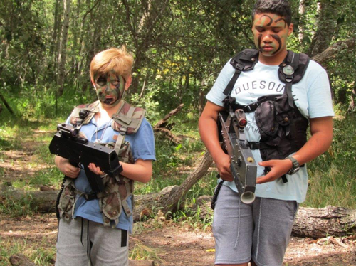Boys in a forest holding laser guns and ready for a fight.  They have the trees and bushes surrounding them.