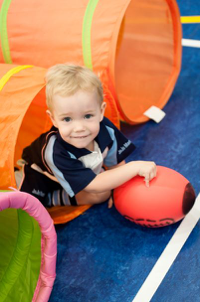 A little boy is holding a rugby ball as he crawls through a tunnel. Fun, structured ball skills for children with rugby tots